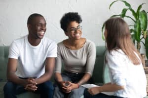 Homme et femme souriants, assis sur un canapé face à une femme.